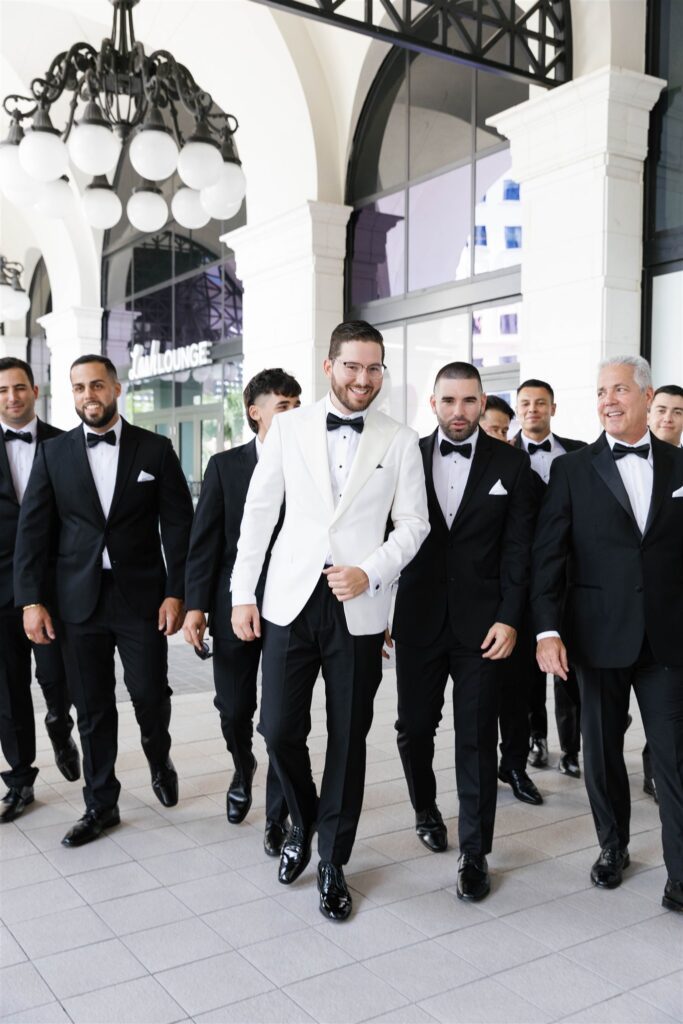 Groom in a white tuxedo jacket walking with his groomsmen