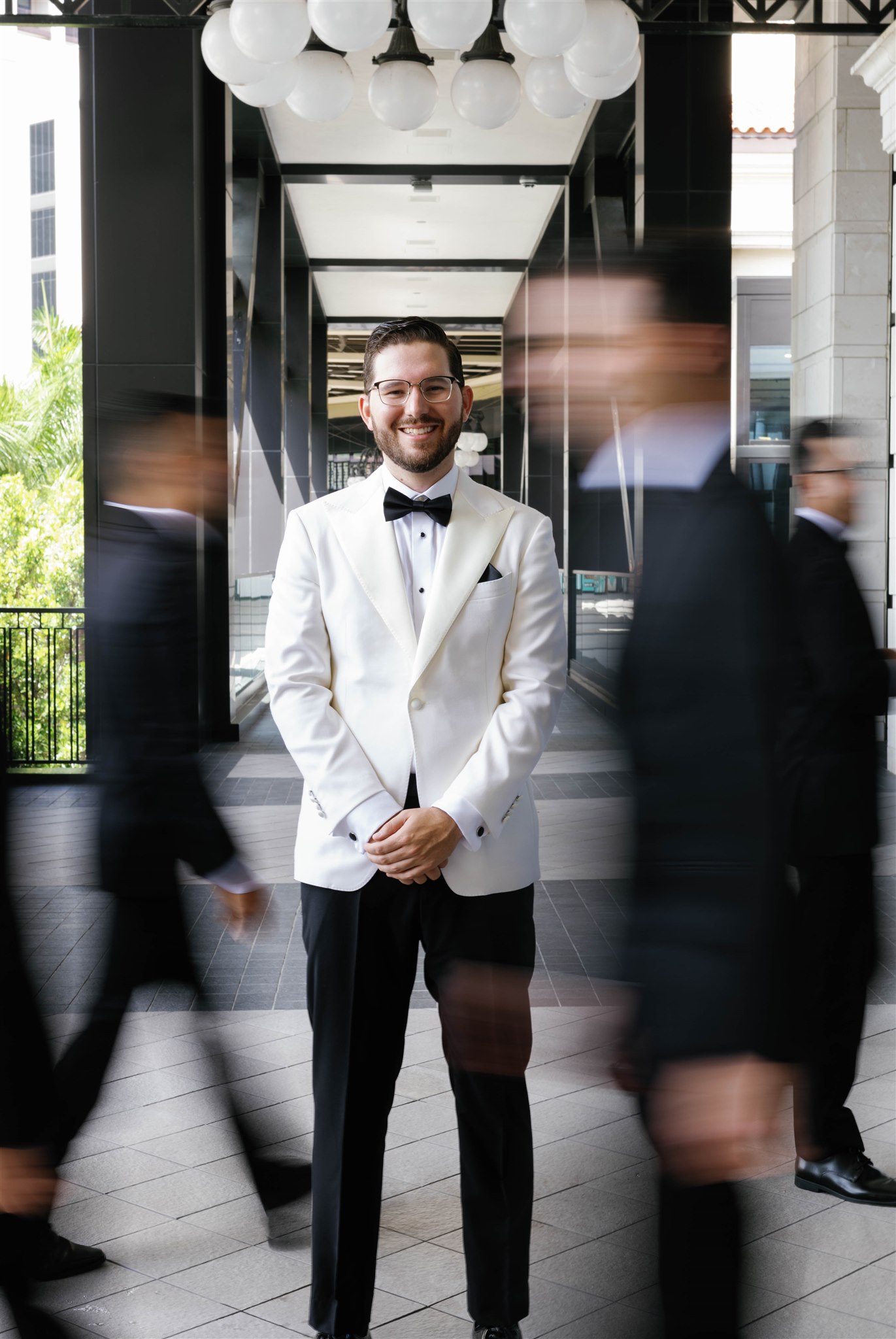 Groom in a white dinner jacket as guests pass by