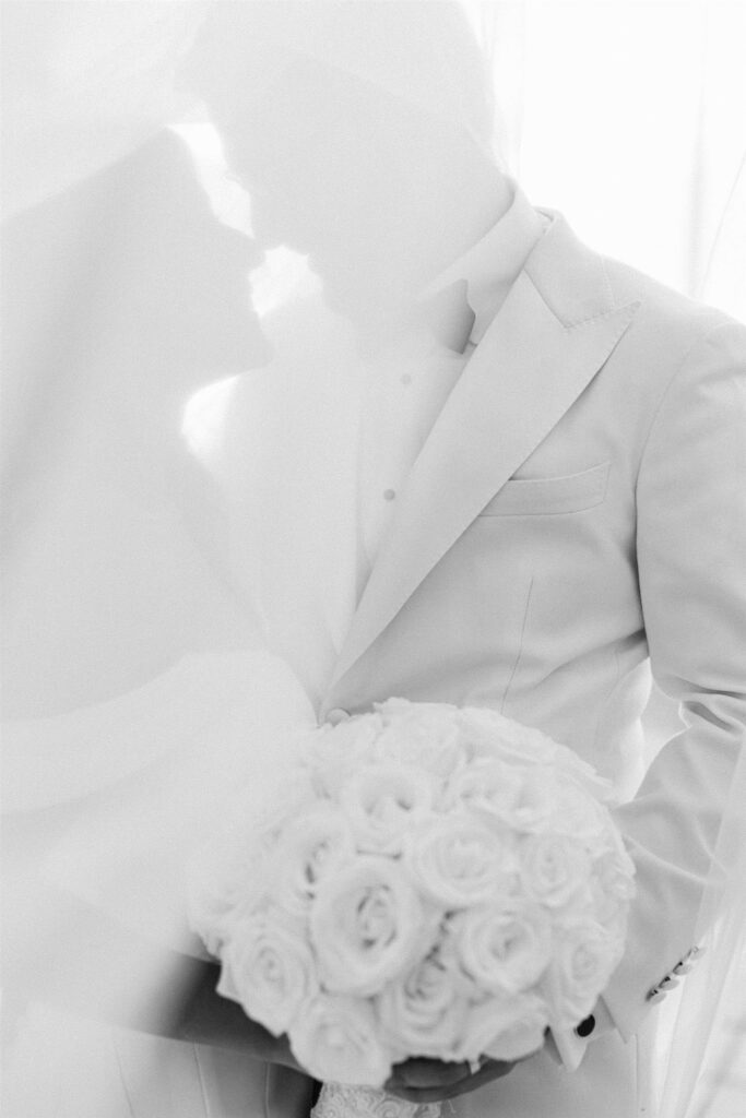 White rose bridal bouquet against the groom's white tuxedo jacket