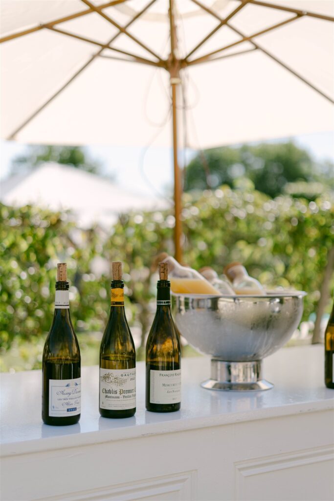 Wine bottles and an ice bucket at the brunch buffet beneath white umbrellas