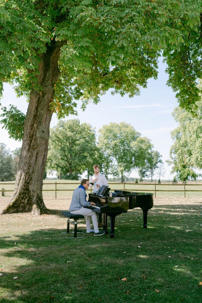 Guests playing the piano on the lawn under a large tree at Château de Varennes