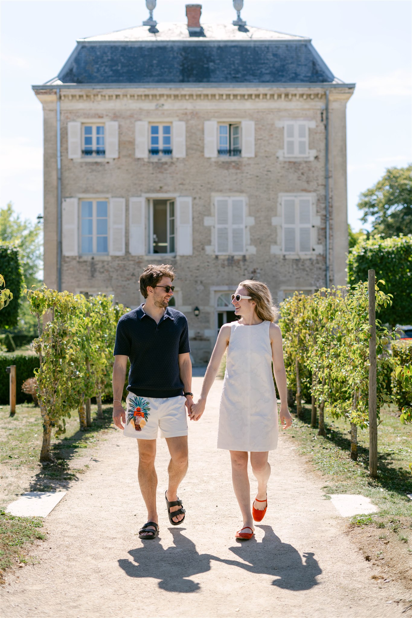 A couple walking hand in hand along the garden path toward the château