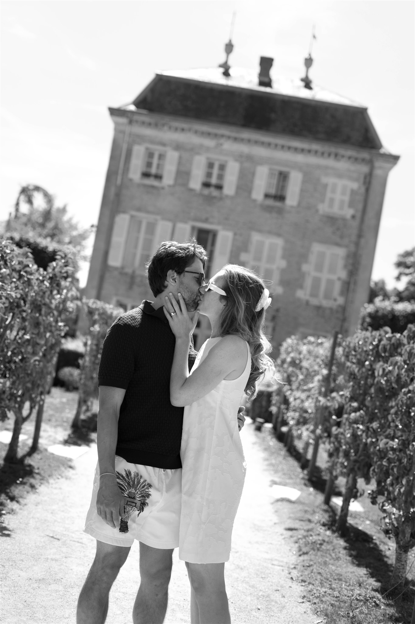 Black and white photo of a couple kissing in the garden in front of the château