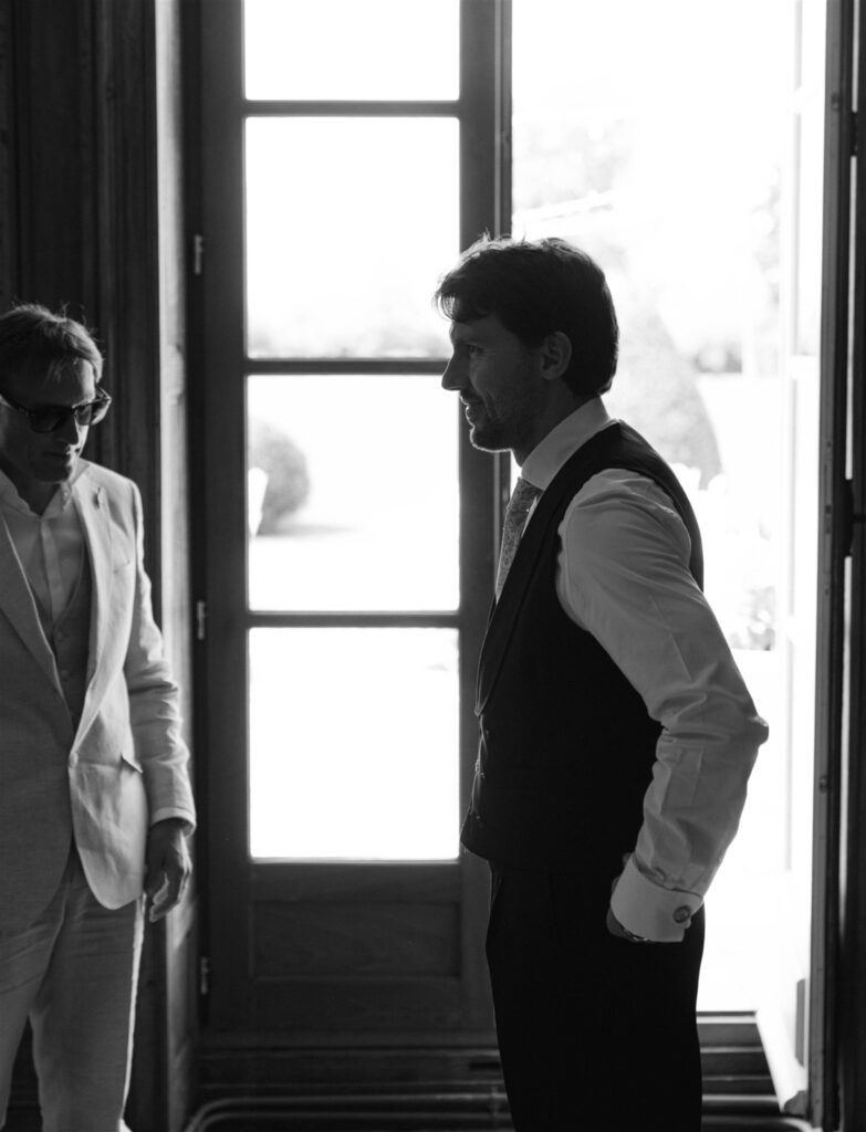 Black and white photo of Jonathan talking with a groomsman by a tall window