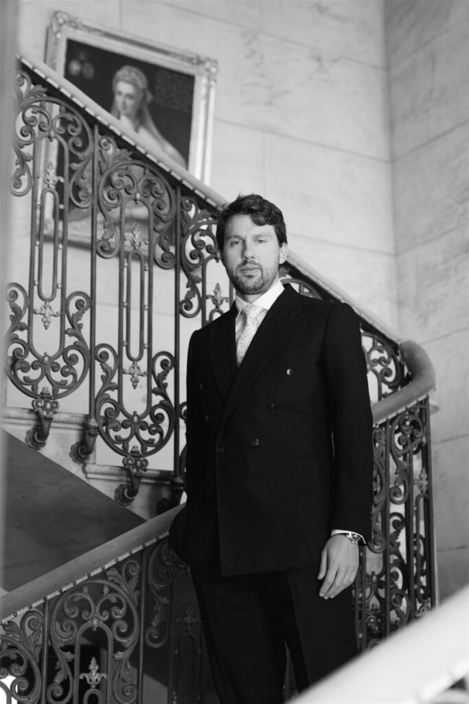 Black and white portrait of Jonathan standing at the wrought-iron staircase railing