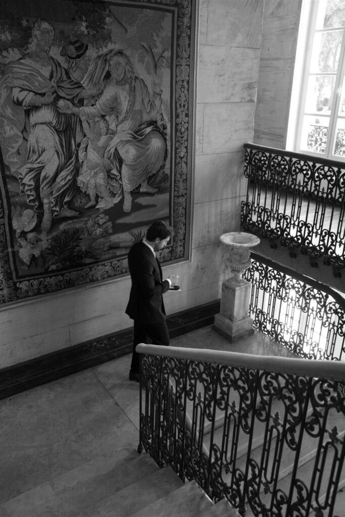 Black and white photo of Jonathan alone on the château staircase with its ornate iron railing