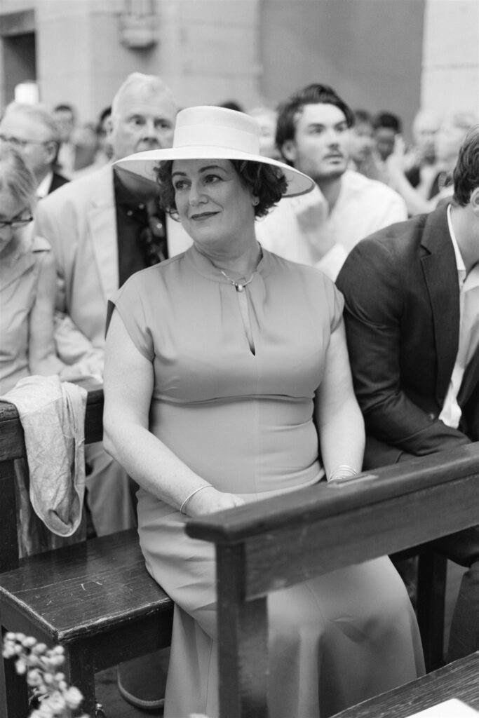Black and white photo of a guest in a wide-brimmed hat watching from the church pews