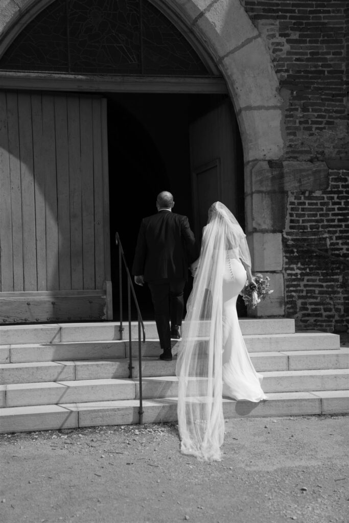Black and white photo of Romy's veil flowing as she stands on the church steps