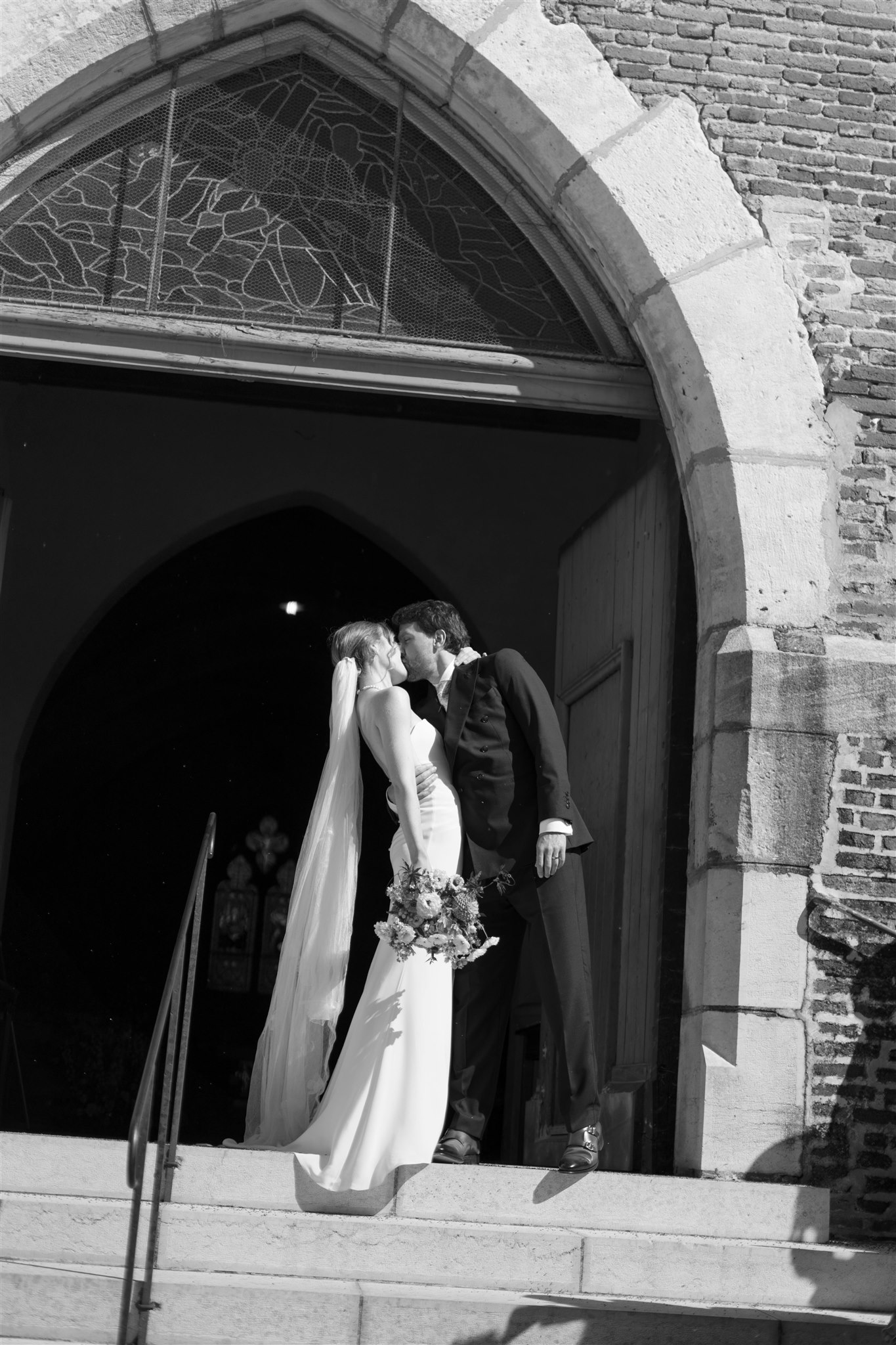 Black and white photo of Romy and Jonathan kissing in the church doorway