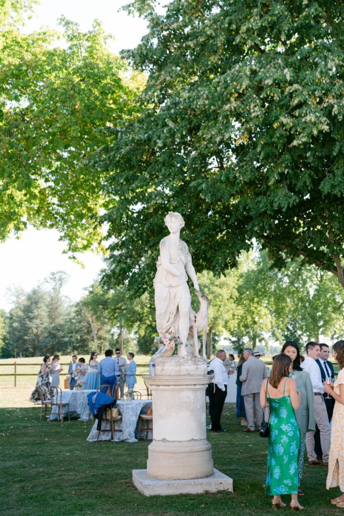 Guests mingling near a marble statue in the château gardens during cocktail hour
