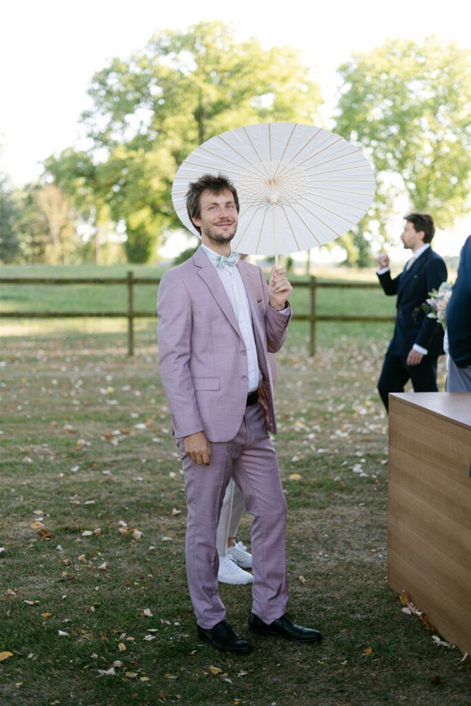 Guest in a lilac suit holding a white parasol in the garden