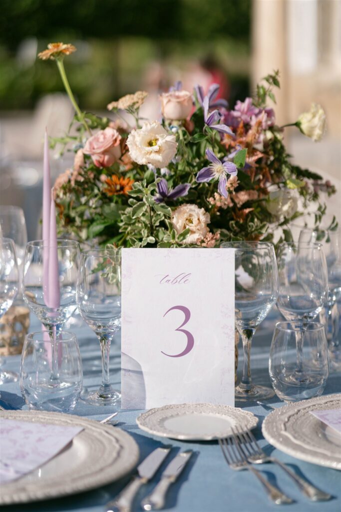 Table number three beside a floral arrangement, candles and blue linen