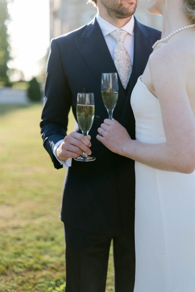 Close detail of Romy and Jonathan holding Champagne flutes, Jonathan in a navy suit