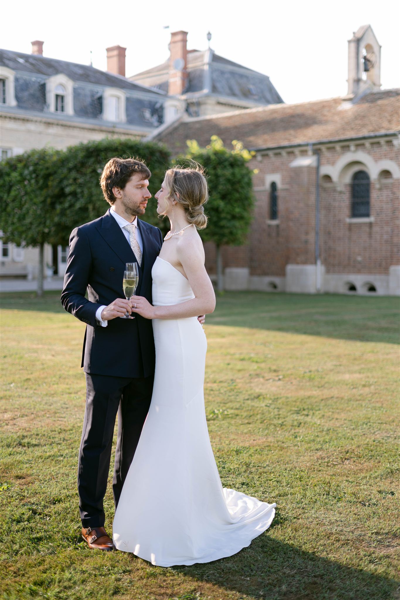 Romy and Jonathan embracing on the lawn in front of the chapel at Château de Varennes in Burgundy