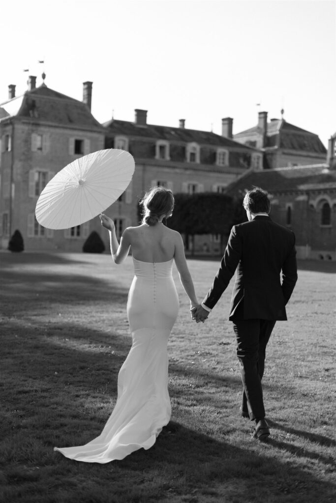 Black and white photo of Romy and Jonathan walking away hand in hand beneath a white parasol
