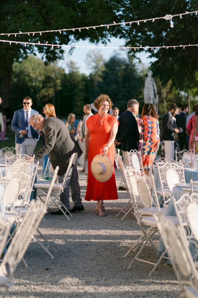 Guests mingling beneath string lights beside white chairs, a woman in a red dress in the center
