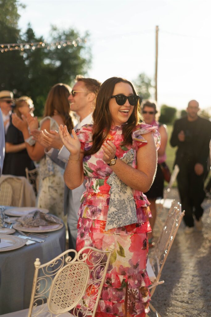 Guest in sunglasses and a pink floral dress clapping at the reception
