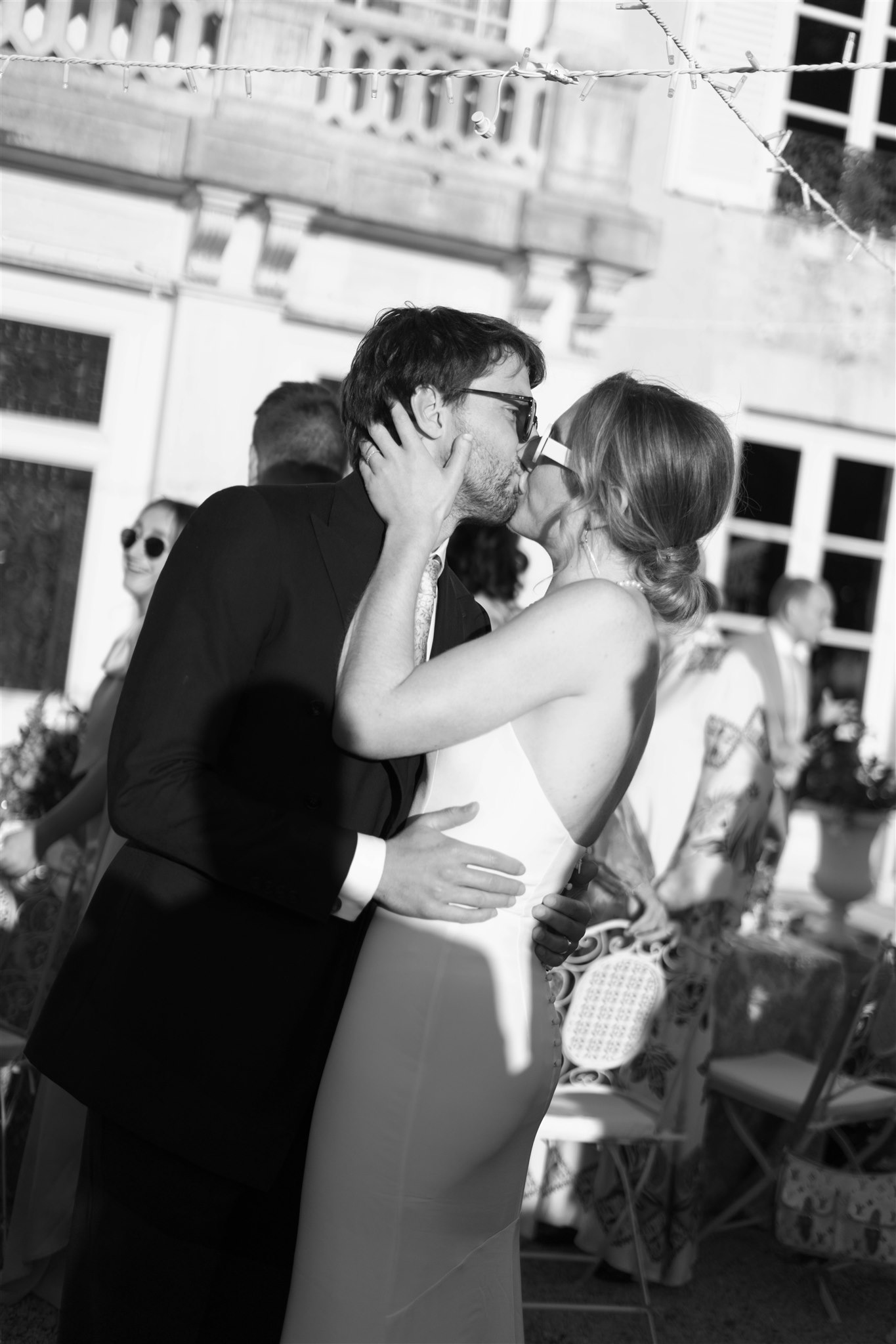 Black and white photo of Romy and Jonathan kissing in front of the château balcony