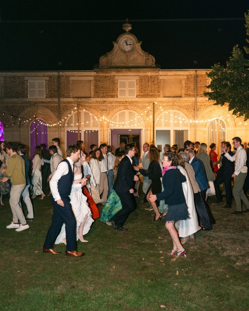 Guests dancing on the château lawn at night, lit by warm lights