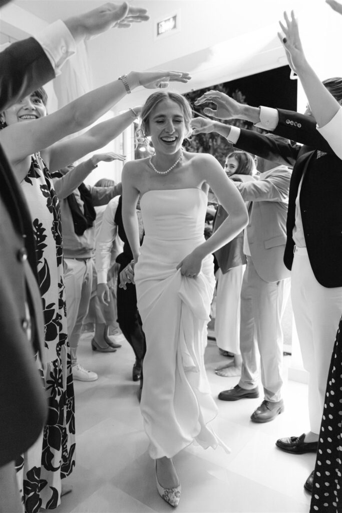 Black and white photo of Romy dancing with her arms raised, guests around her