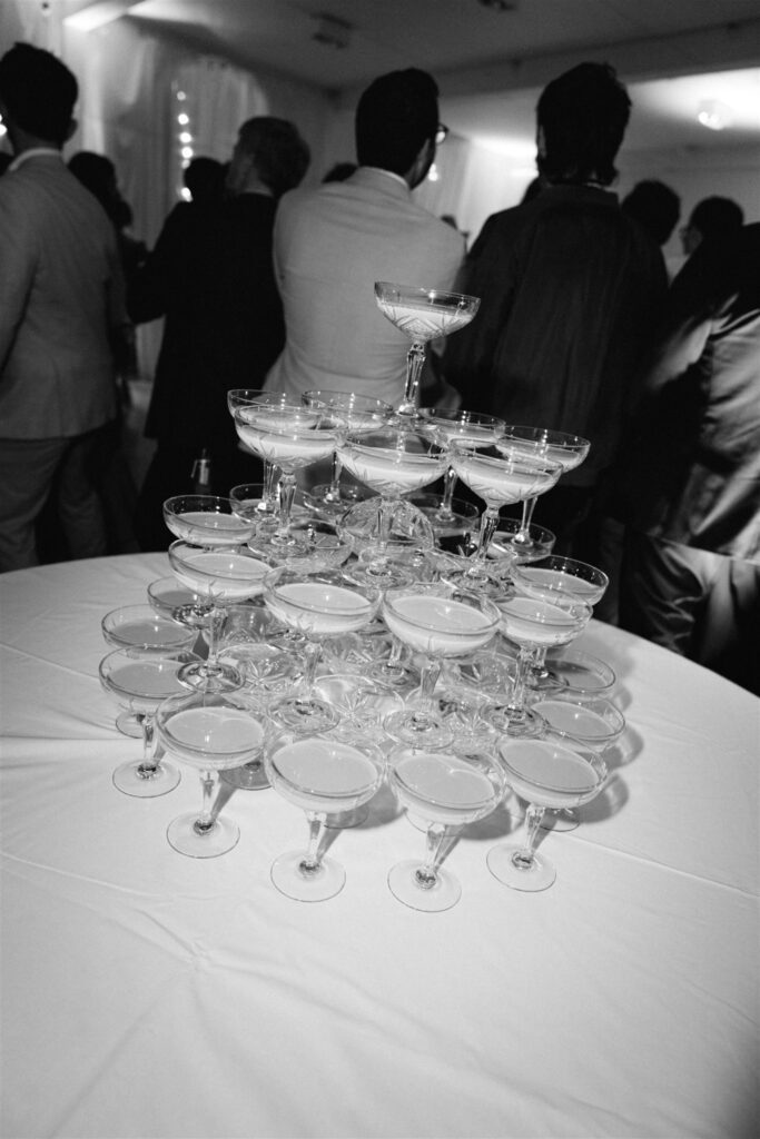 Black and white photo of a tower of coupe glasses on a reception table