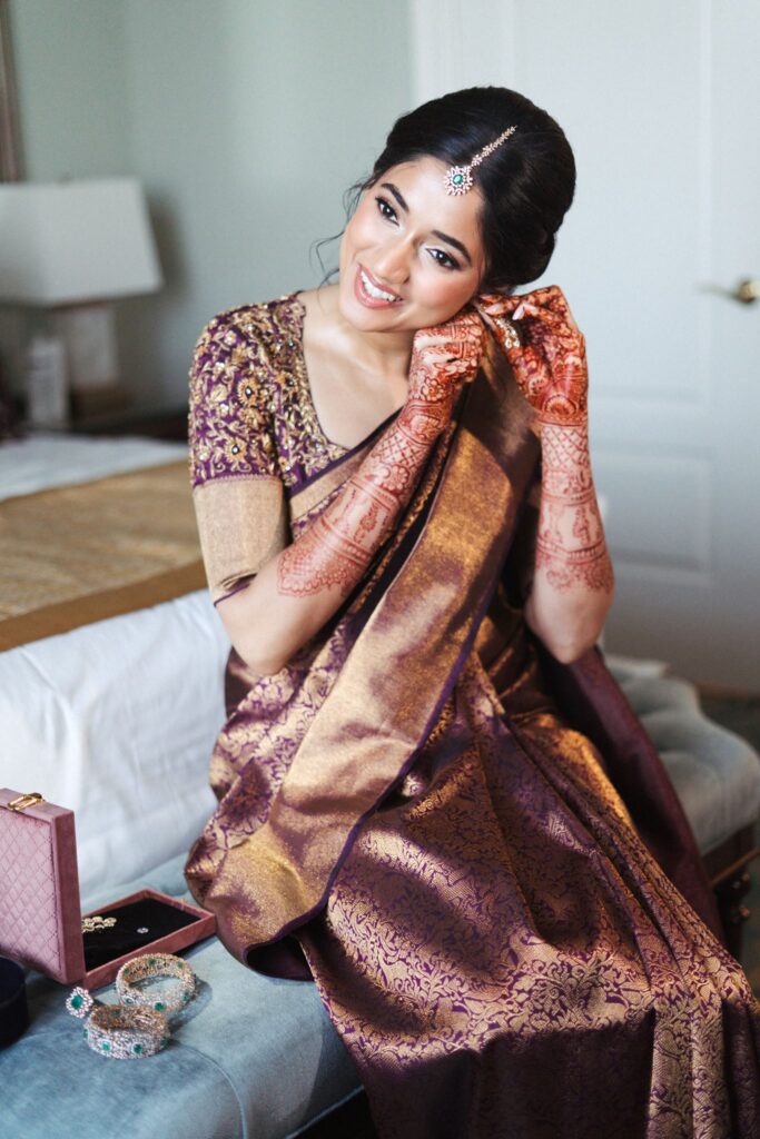 Bride touching her earring while seated in her purple and gold saree  at The Biltmore Hotel