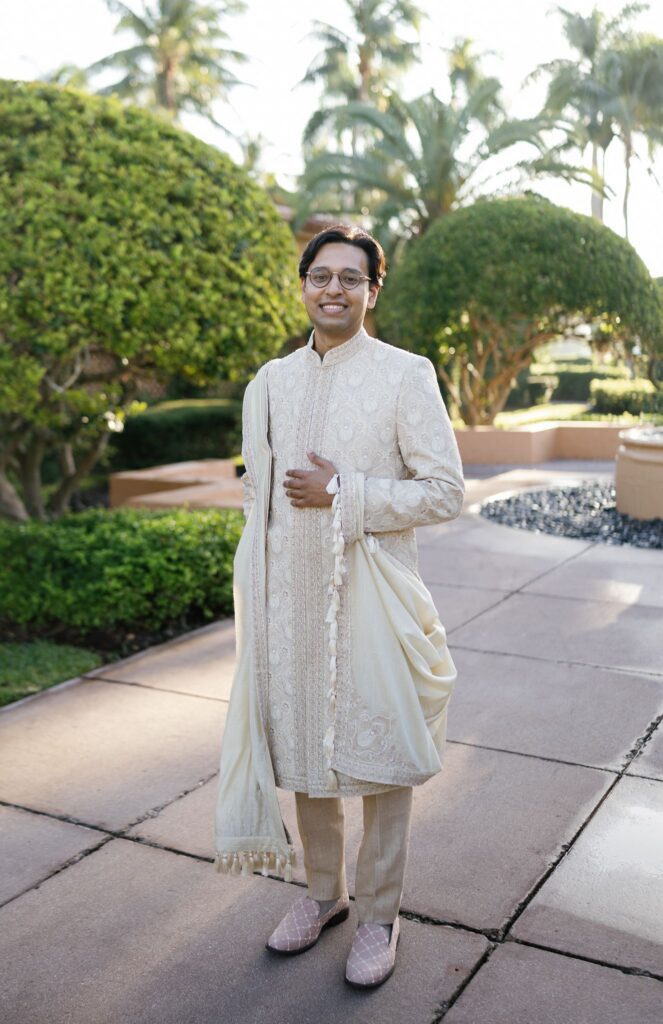 Tejus in an ivory and gold sherwani standing among manicured hedges