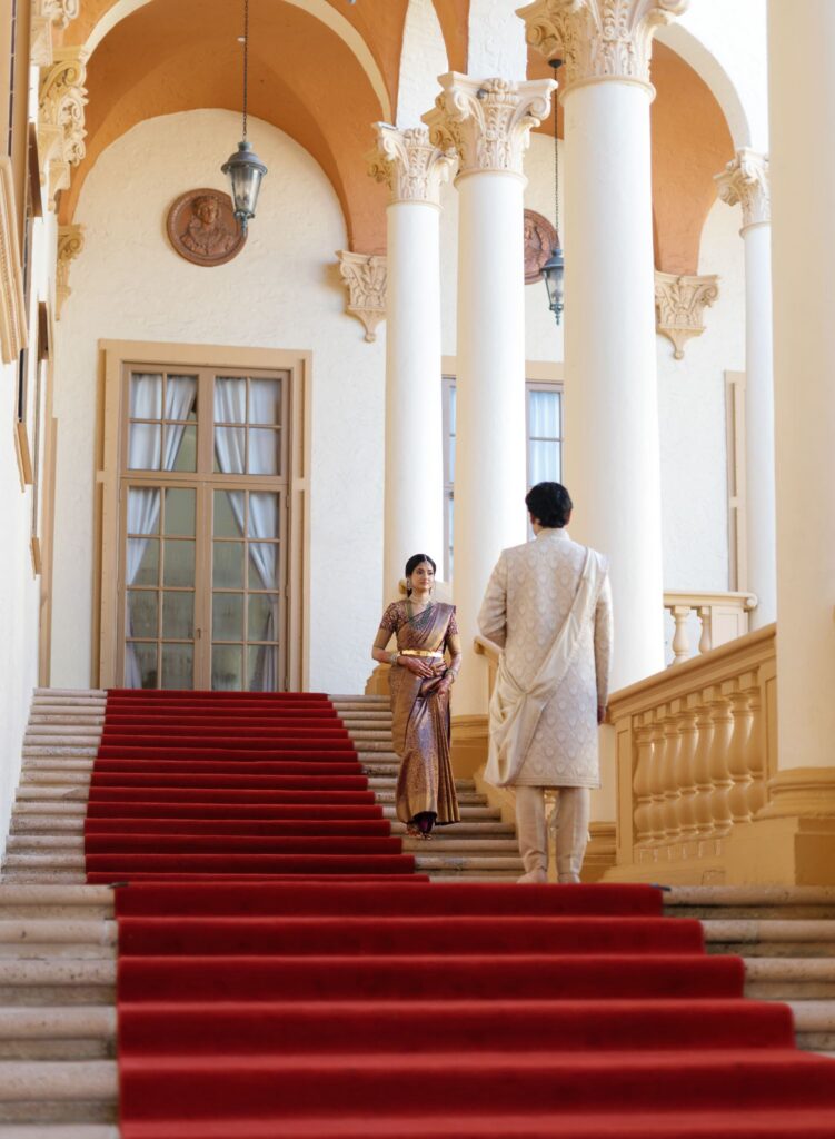 Groom waiting in the middle of the red-carpeted Biltmore staircase as Bride descends for their first look