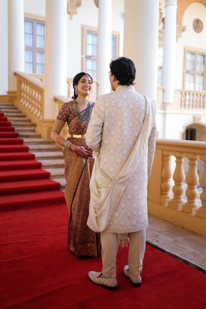 Advaitaa and Tejus facing each other on the red-carpeted staircase after their first look