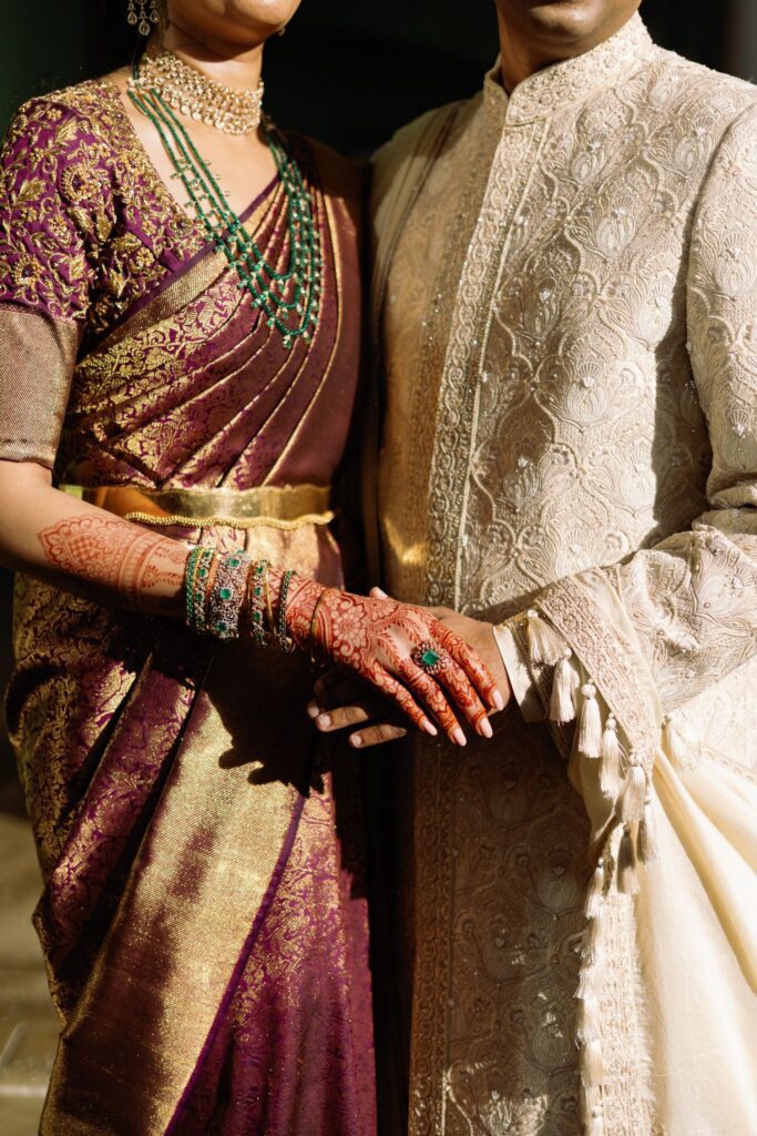 Close-up of the couple's clasped hands, her henna and the embroidered sherwani