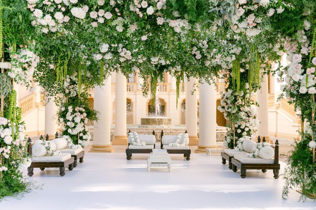 Mandap covered in hanging greenery and white roses with seating below