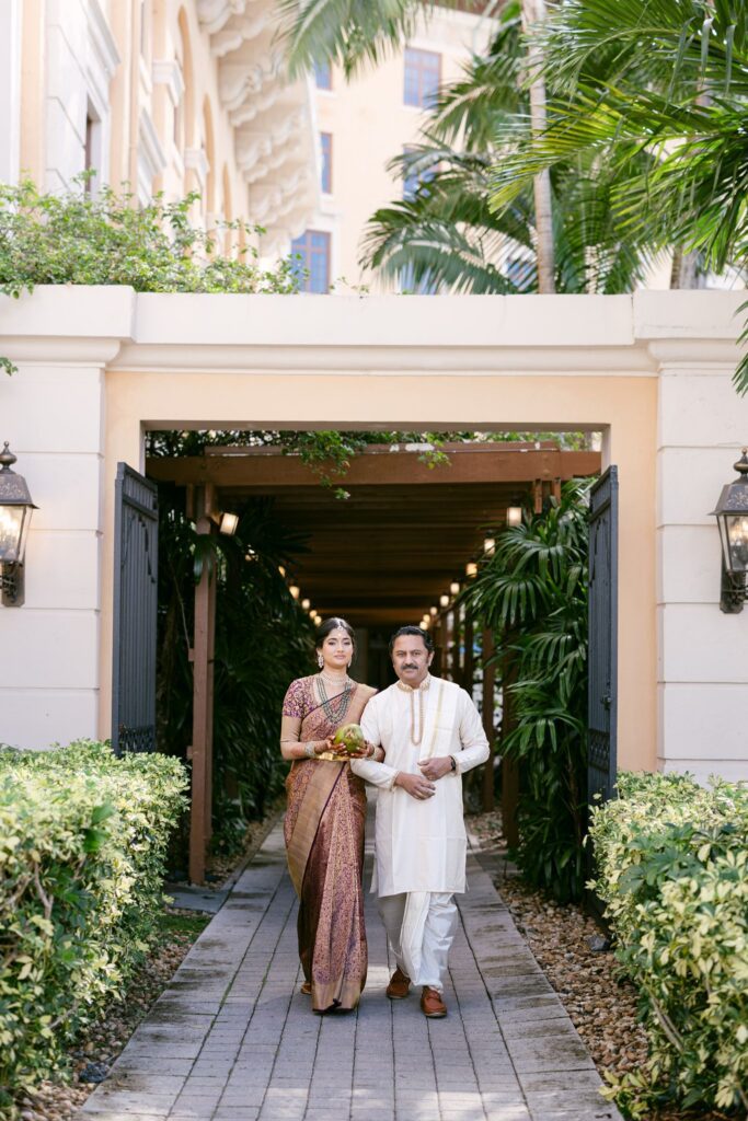 Tejus and Advaitaa walking together through a lantern-lit passage to the ceremony