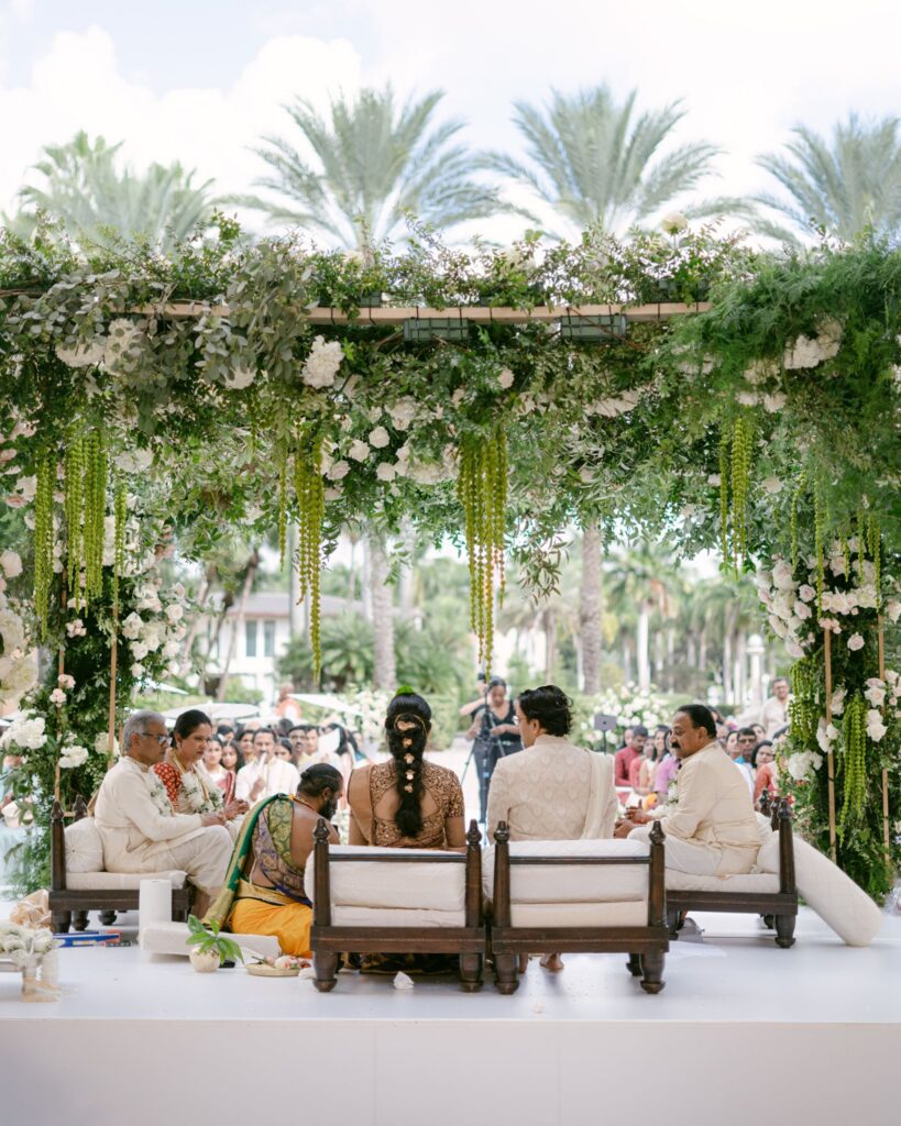 Wide view of the couple and priest under the greenery-covered mandap