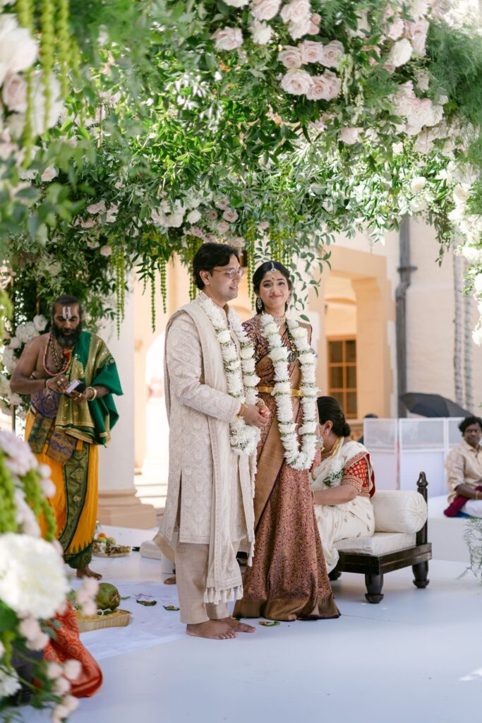 Couple standing together in garlands in front of the ritual fire