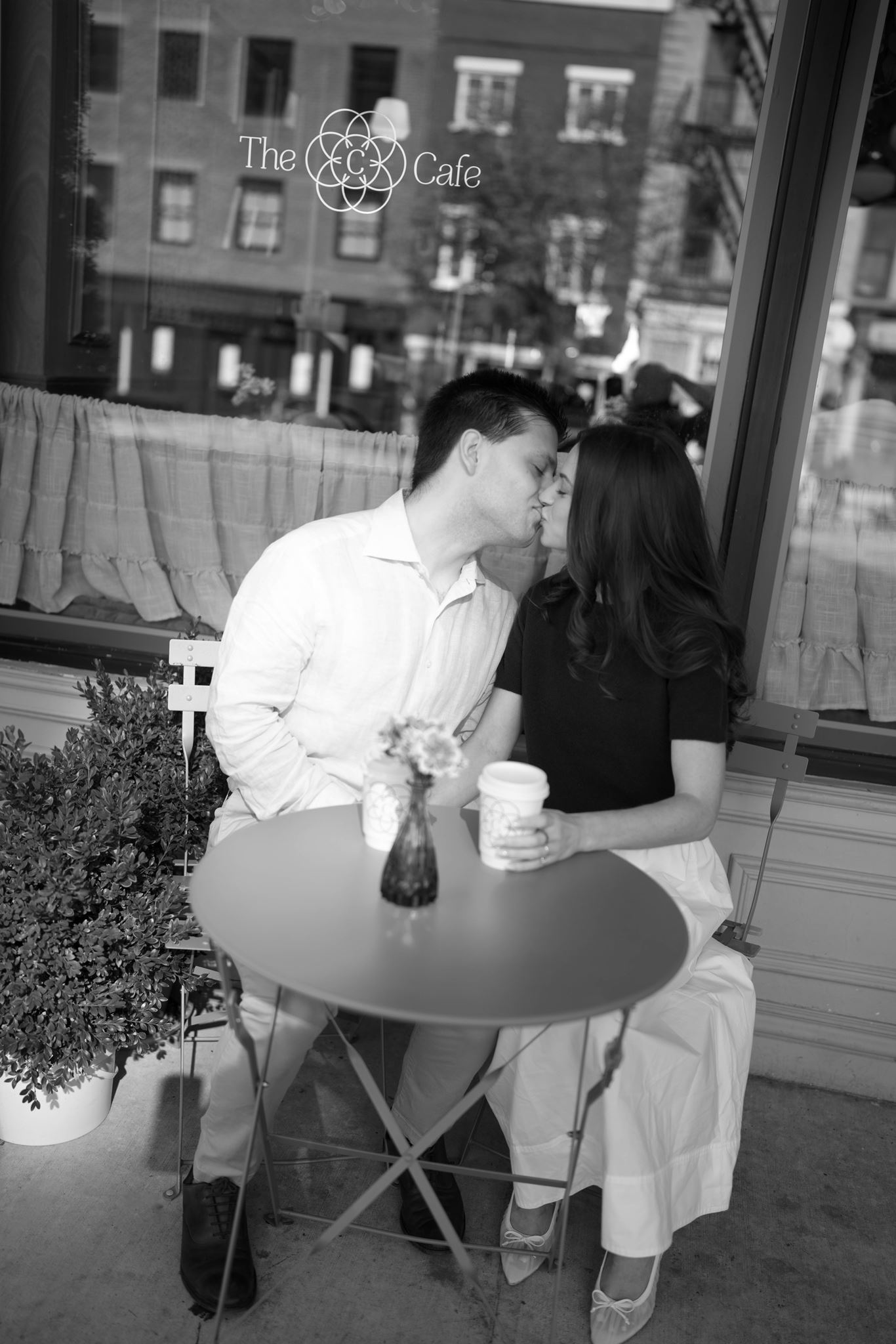 Haley and Jeremy sitting at a small green bistro table outside a West Village café during their New York City engagement session