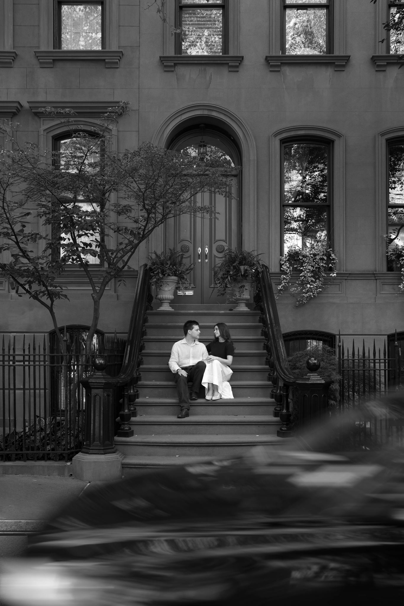 Black and white portrait of Haley and Jeremy laughing together on a brownstone stoop