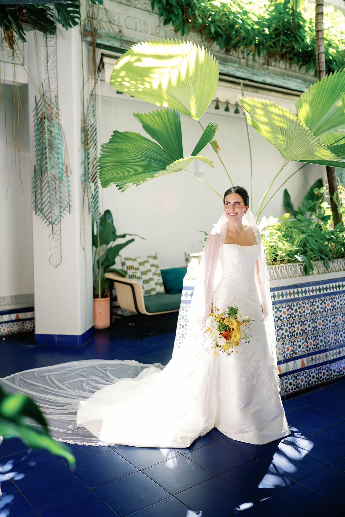 Ashley in her veil standing in a sunlit courtyard with blue tile and palm leaves