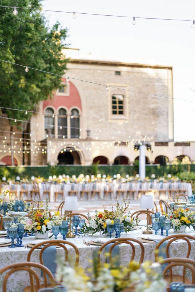 Reception tables with blue goblets, woven chargers and yellow florals overlooking The Deering Estate
