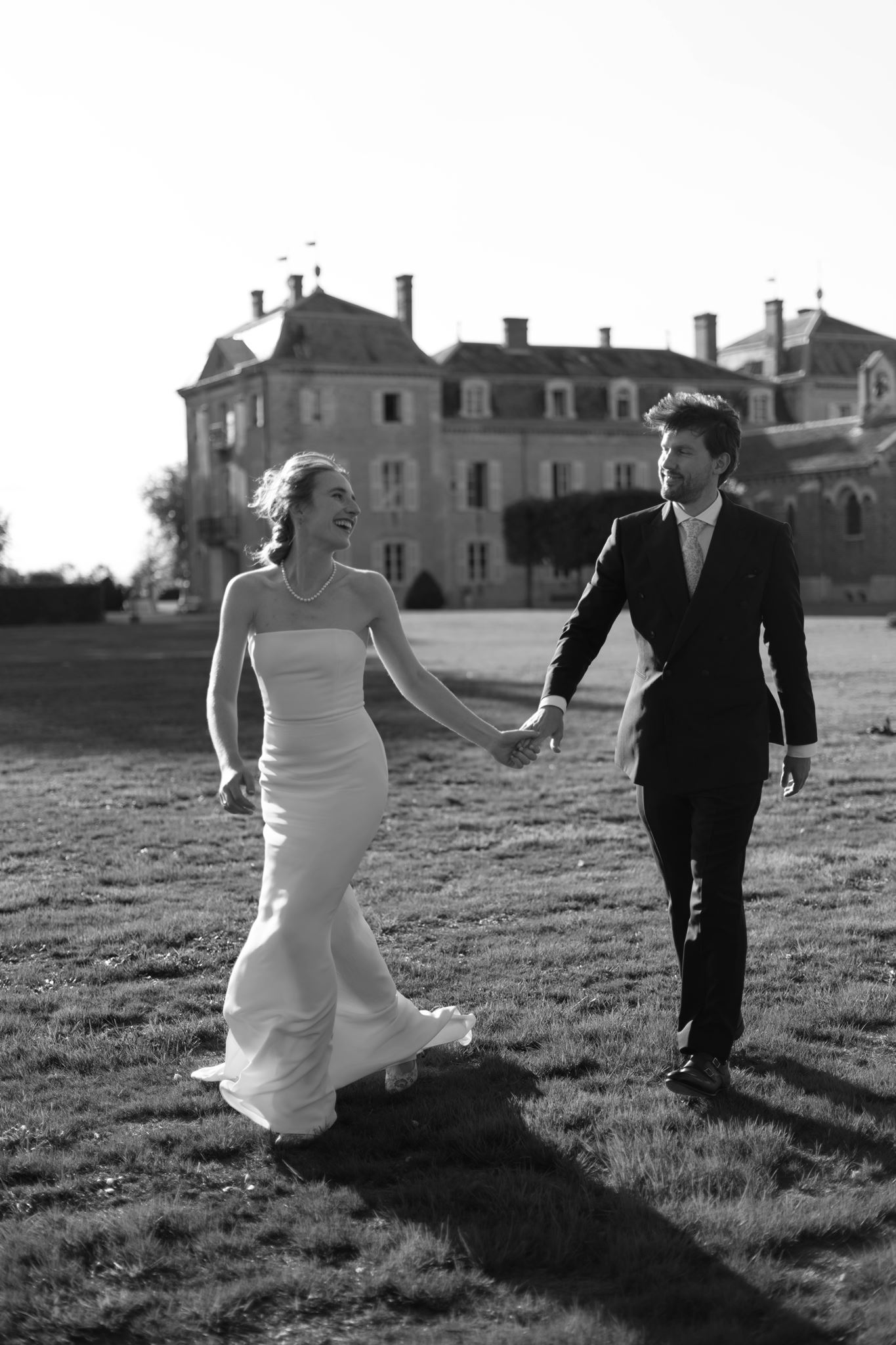 Black and white photo of Romy and Jonathan walking across the lawn in front of the château
