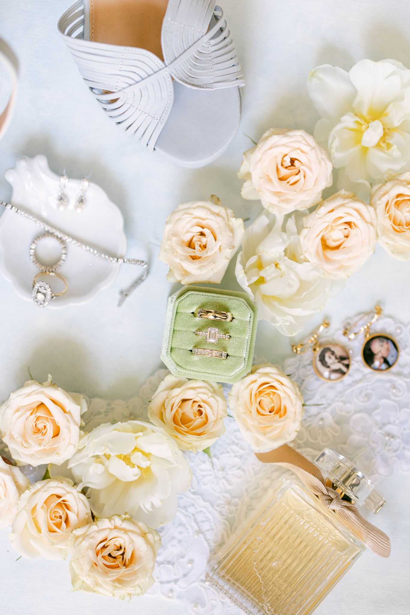 Bridal details with white heels, perfume, wedding rings and cream roses