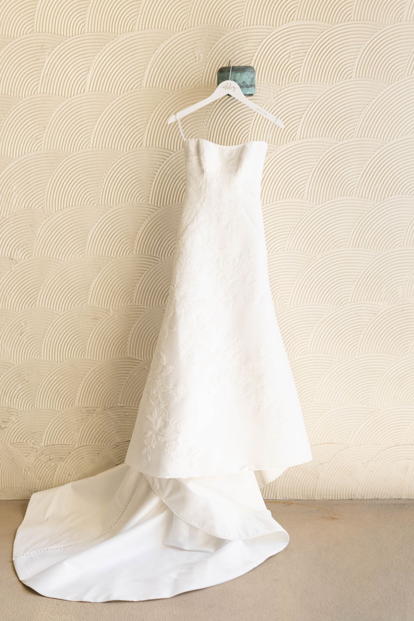 Ashley's A-line wedding gown with subtle floral embroidery and a long train hanging in the hotel suite