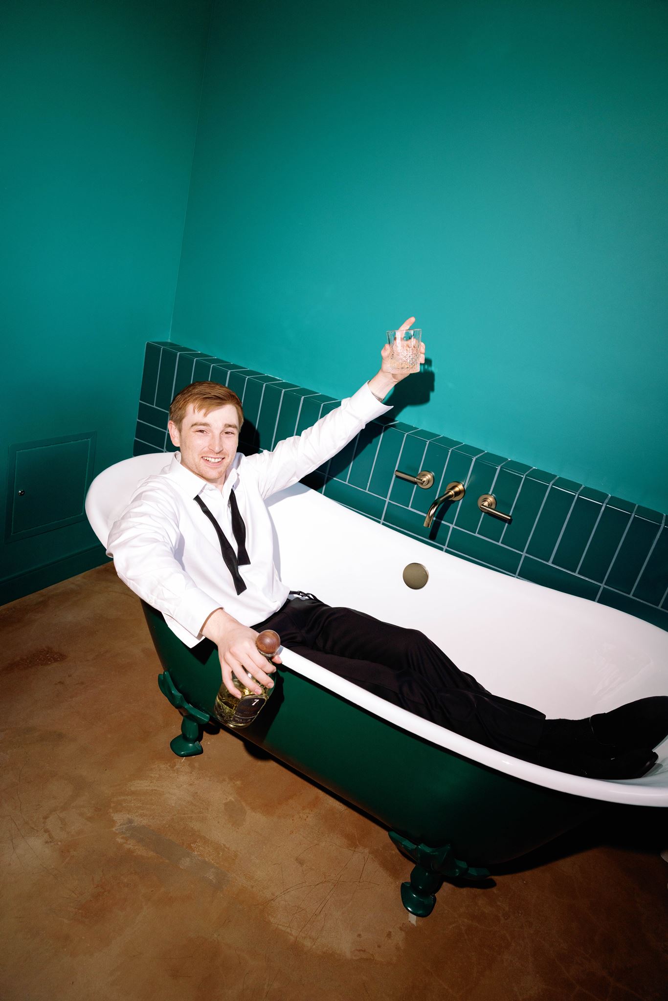 Luke relaxing in a clawfoot bathtub in his white shirt and bow tie before the wedding