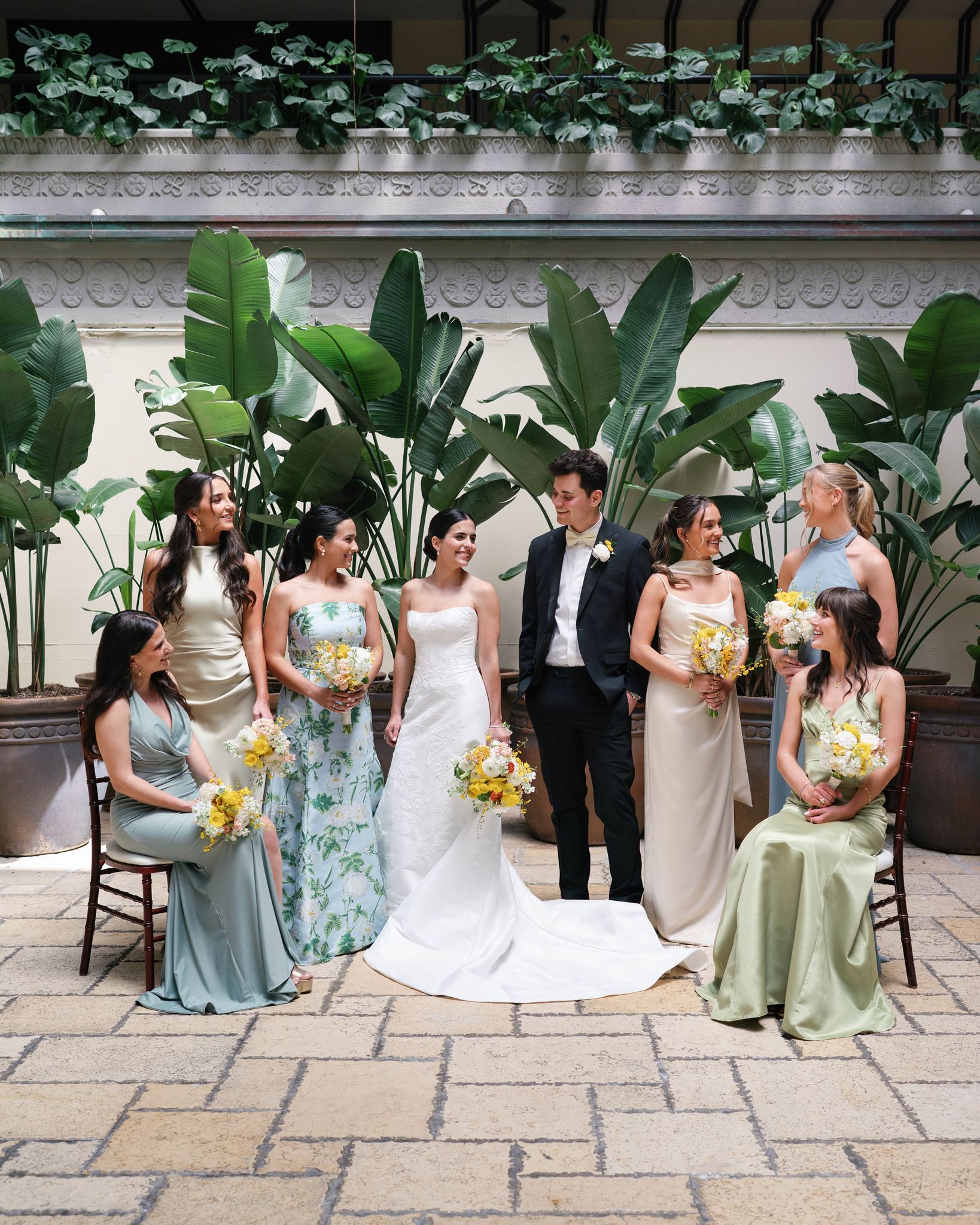 Ashley and Luke with their bridal party in a hotel courtyard surrounded by banana leaves