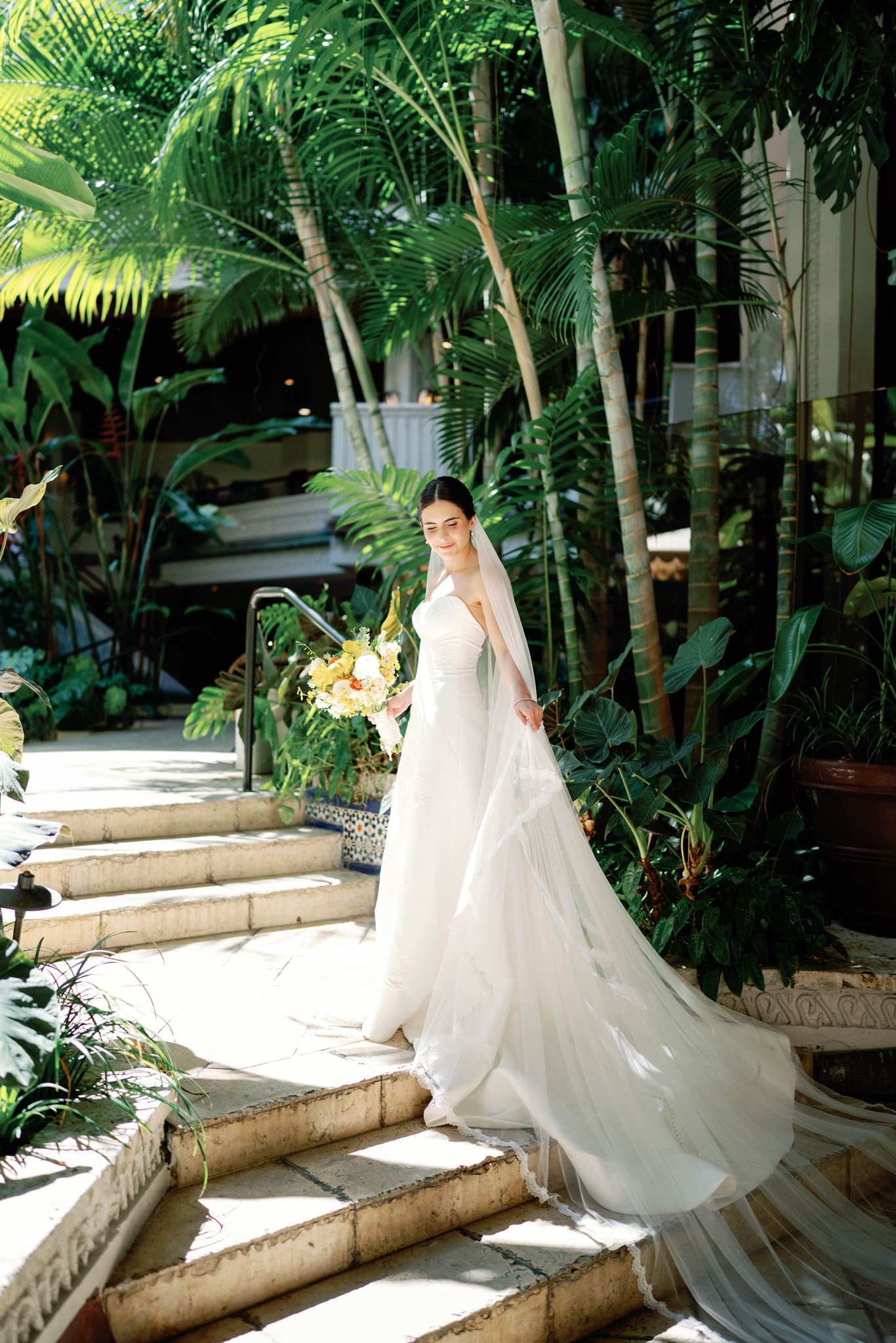 Ashley in her cathedral-length veil on stone steps surrounded by tropical plants