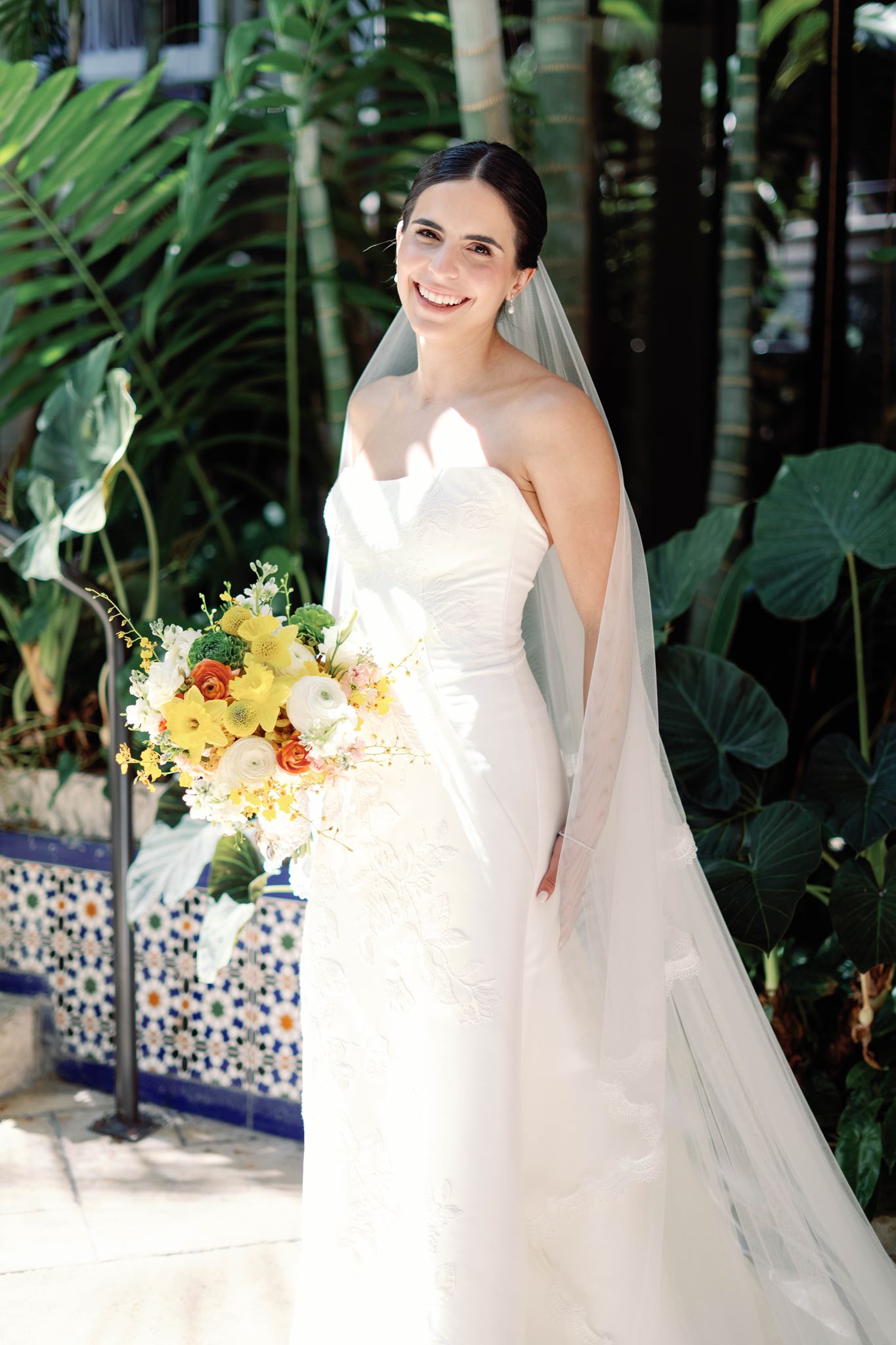 Ashley smiling and holding a yellow and white bouquet in her veil