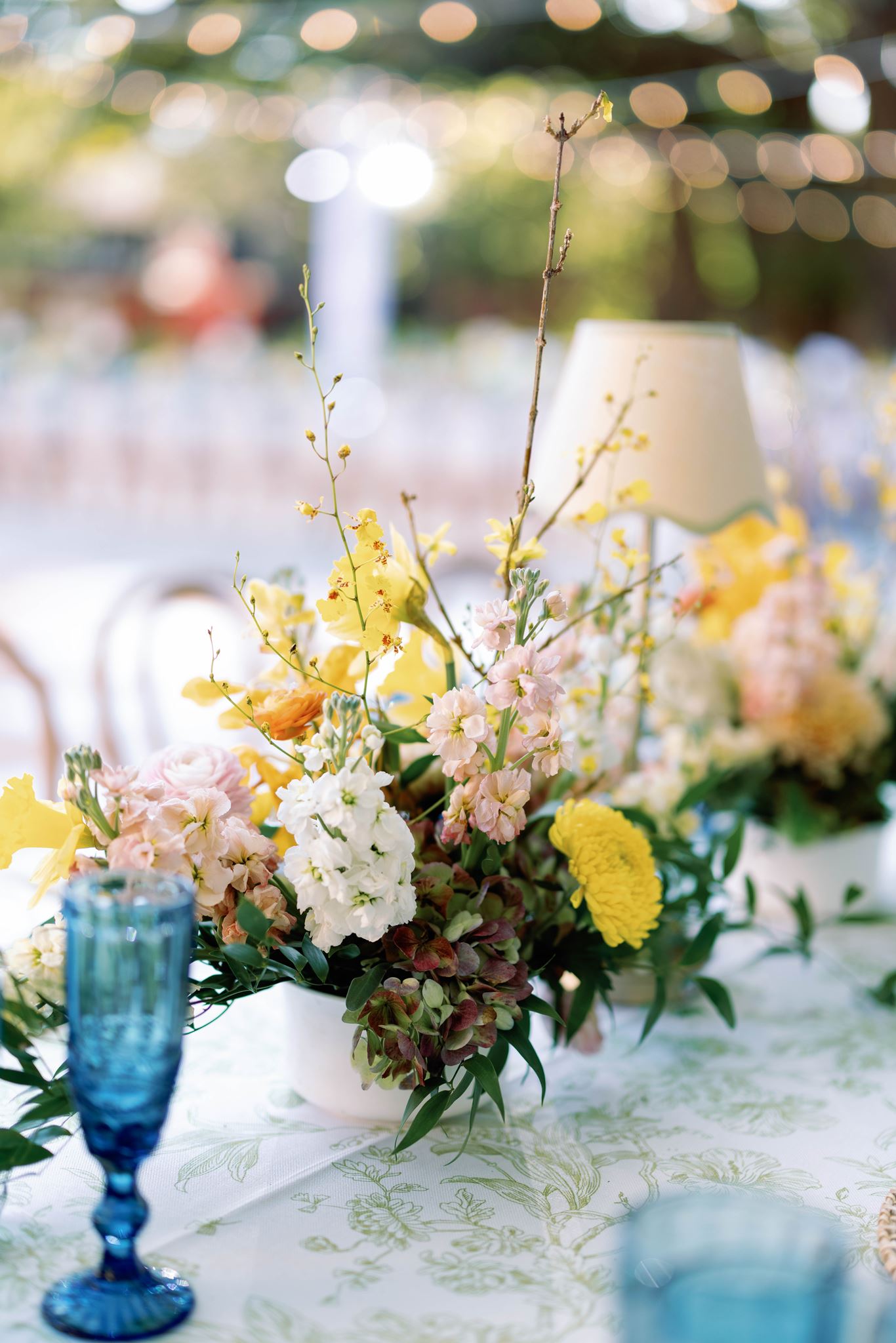 Yellow and white floral centerpiece beside a blue goblet at the reception