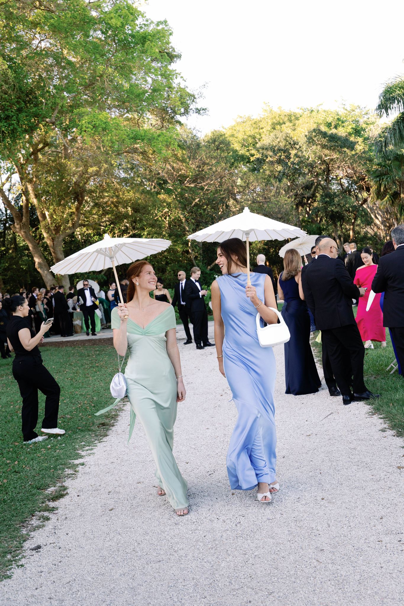 Two guests walking with parasols along a gravel path at cocktail hour