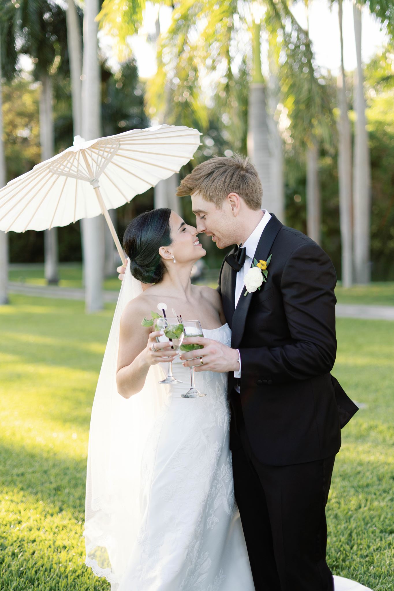 Ashley and Luke smiling under a paper parasol holding mojitos
