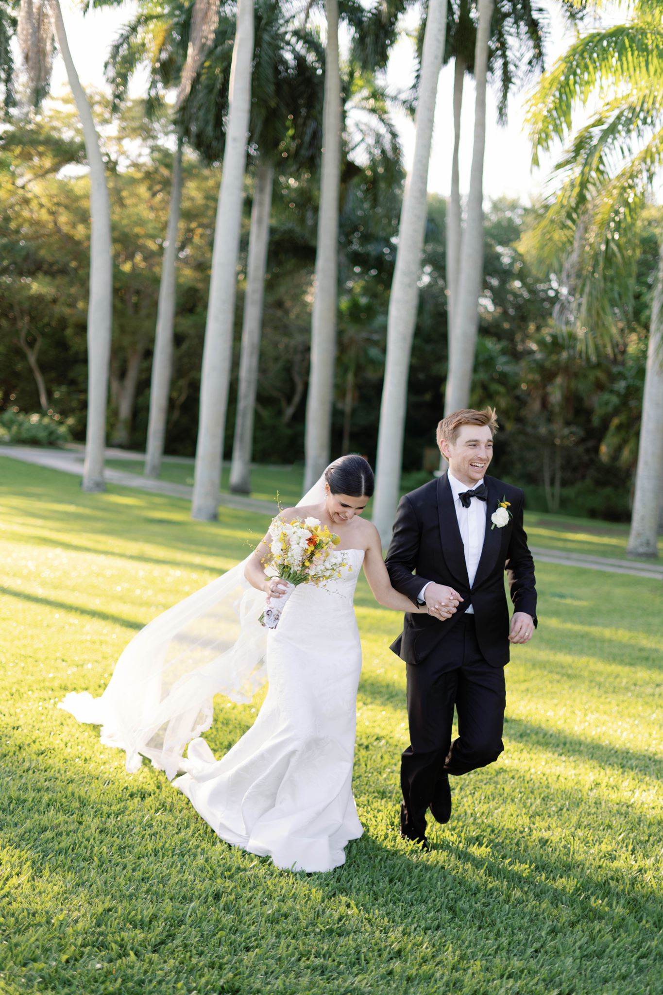 Ashley and Luke walking and laughing through the palm trees at the Deering Estate