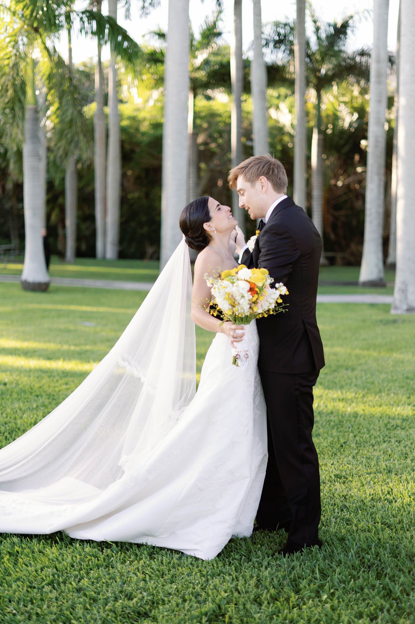 Ashley and Luke embracing on the lawn as her veil flows behind them
